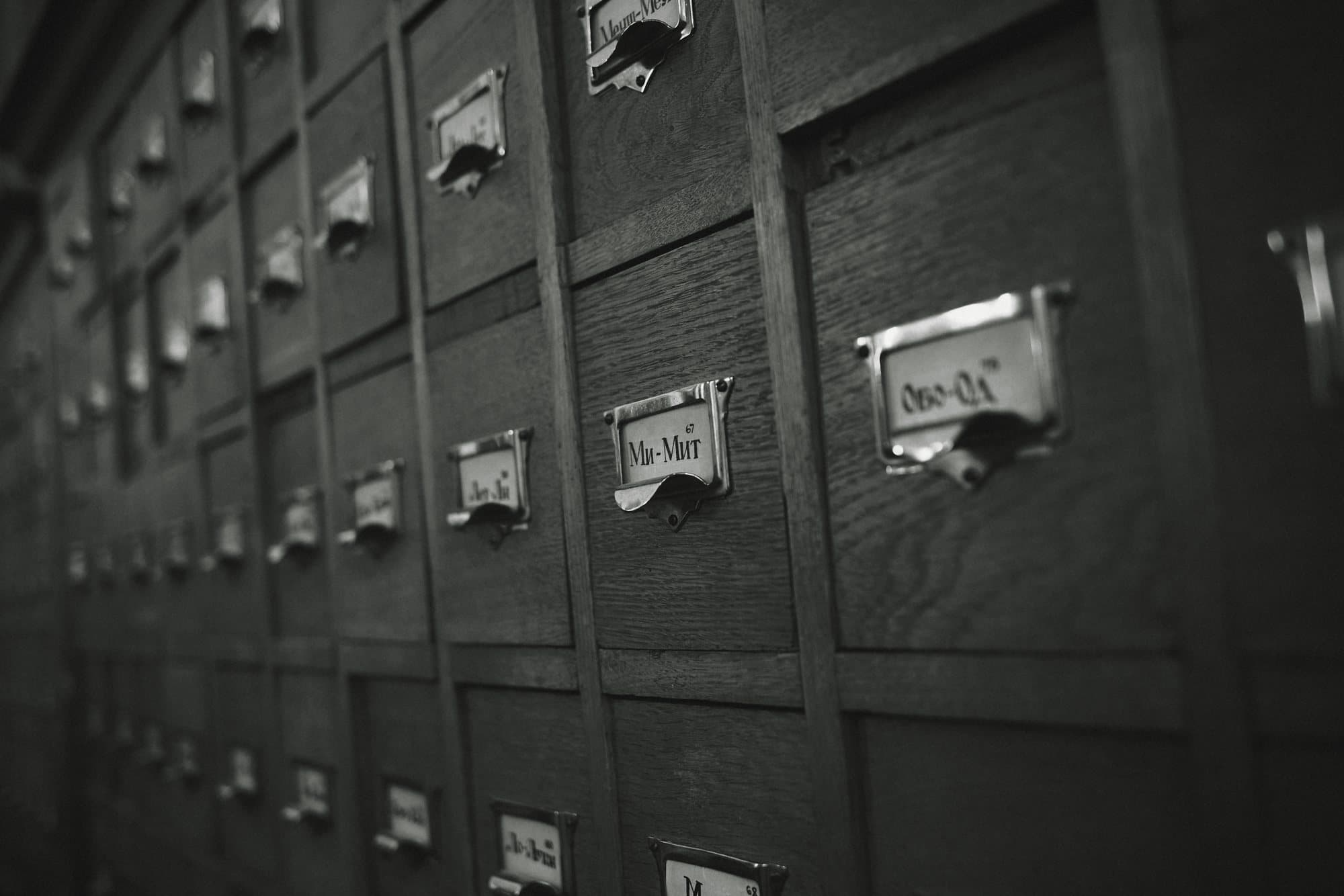 Rows of wooden card-catalogue drawers with metal label holders, in black and white.